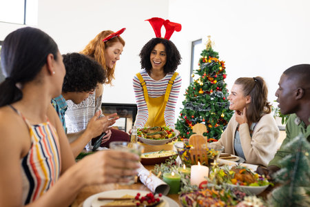 Happy diverse friends sitting at table and having dinner at christmas. Christmas, celebration, friendship, inclusivity and lifestyle concept.の写真素材