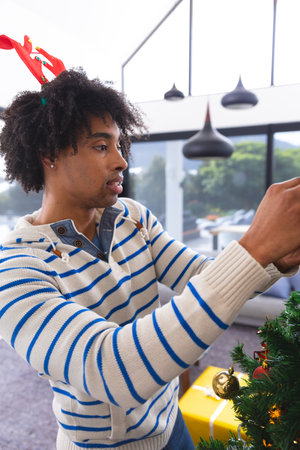 Happy african american man decorating christmas tree in living room. Spending quality time at christmas together.の写真素材