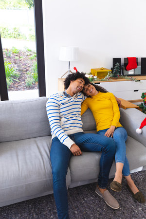 Happy african american couple sitting on sofa in living room and embracing. Spending quality time at christmas together.の写真素材
