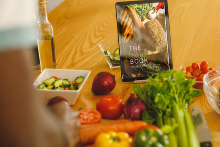 Hands of african american man using recipe on tablet preparing food in kitchen. Communication, domestic life, health and inclusivity concept.の写真素材