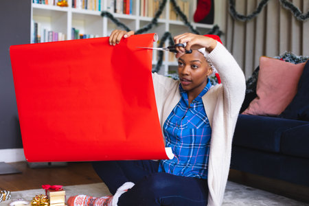 Happy african american woman wearing santa claus hat, packing presents. Spending quality time at christmas alone.の写真素材