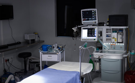 Electronic medical equipment with monitor screens on and empty operating table in operating theatre....