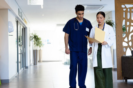 Diverse male and female doctor with folder discussing walking in hospital corridor, with copy space. Hospital, medical and healthcare services.の写真素材