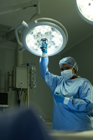 Vertical of biracial female surgical tech adjusting light in operating theatre, with copy space....