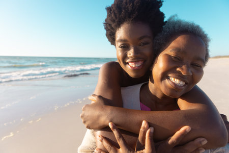 Portrait of african american loving young woman embracing senior mother at beach against sea and sky. Copy space, unaltered, family, summer, together, vacation, retirement, enjoyment and nature.の写真素材