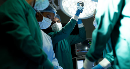 Biracial male surgical tech adjusting light for colleagues during operation in operating theatre....