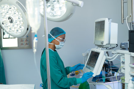 Side view of biracial female surgeon operating computerised medical equipment in operating theatre. Hospital, medical and healthcare services.の写真素材