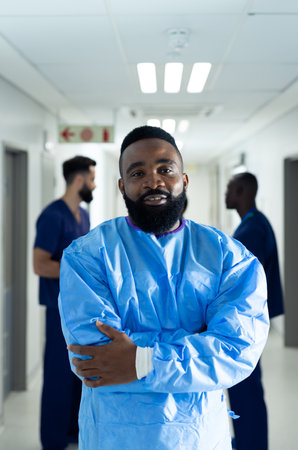 Vertical portrait of smiling biracial male healthcare worker in busy hospital corridor, copy space. Hospital, medical and healthcare services.の写真素材