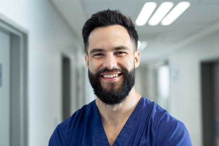 Portrait of smiling bearded caucasian male healthcare worker in hospital corridor, copy space. Hospital, medical and healthcare services.の写真素材