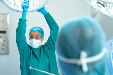 Biracial female surgeon and colleague adjusting lights in operating theatre for operation. Hospital, medical and healthcare services.の写真素材