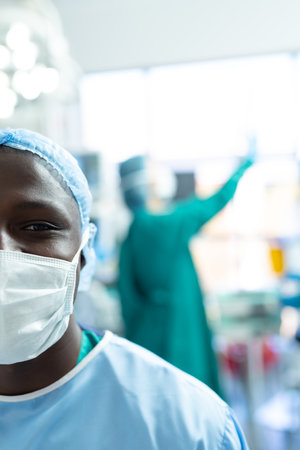 Vertical half portrait of smiling african american male surgeon in mask in theatre, with copy space. Hospital, medical and healthcare services.の写真素材