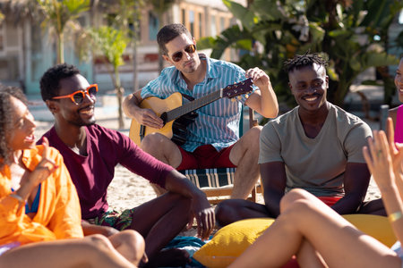 Happy diverse friends playing guitar at beach. Spending quality time, lifestyle, friendship,...