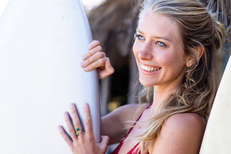 Happy caucasian woman holding surfboard at beach. Spending quality time, lifestyle, summertime and vacation concept.の写真素材