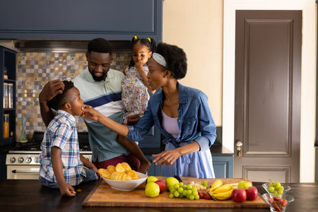 African american mother feeding fresh fruits to children and husband while standing in kitchen. Copy space, unaltered, family, togetherness, childhood, lifestyle and home conceptの写真素材