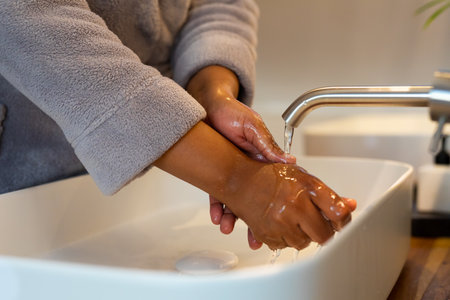 Midsection of plus size african american woman wearing robe, washing hands in bathroom. Self care, domestic life, body inclusivity and lifestyle, unaltered.の写真素材