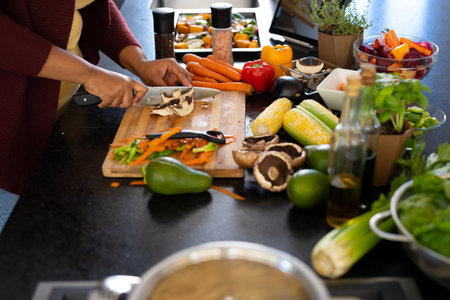 Midsection of plus size african american woman preparing dinner, chopping vegetables in kitchen....