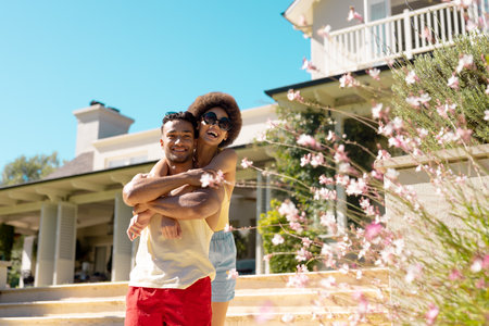 Portrait of happy diverse couple standing outside the house, embracing and smiling. Lifestyle, friendship, party time, vacation and summer.の写真素材