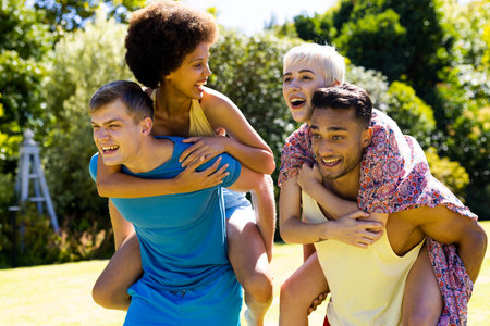 Happy diverse group of friends giving each other piggyback rides in garden. Lifestyle, friendship,...