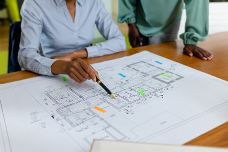Midsection of african american female architects analyzing blueprint on desk in office, copy space....