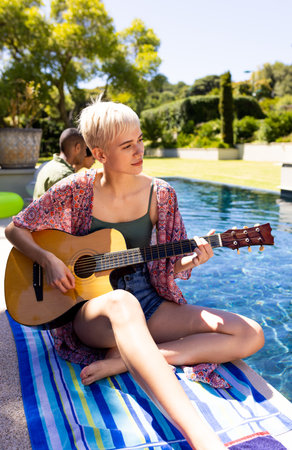 Happy caucasian woman having pool party, playing guitar and smiling in garden. Lifestyle, party and...