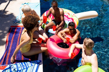 Happy diverse group of friends having pool party, holding plastic cups in garden. Lifestyle,...