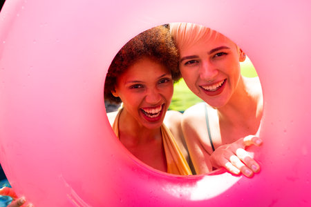 Portrait of happy diverse female friends having pool party, holding swim ring and smiling in garden. Lifestyle, friendship, party and summer.の写真素材