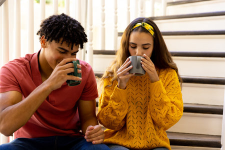 Happy diverse couple sitting on stairs at home drinking coffee. Free time, relaxation, togetherness...