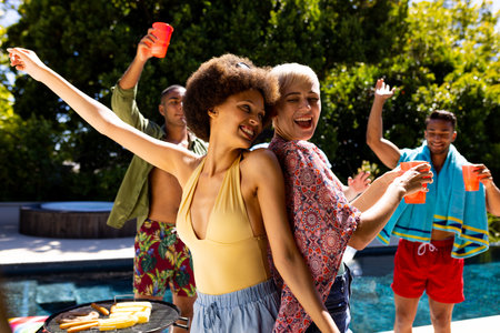 Happy diverse group of friends having pool party, barbecuing and dancing in garden. Lifestyle, friendship, party and summer.の写真素材