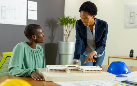 African american female architects discussing new project over model on table in office, copy space. Unaltered, architecture, construction industry, short hair, design, teamwork and business concept.の写真素材