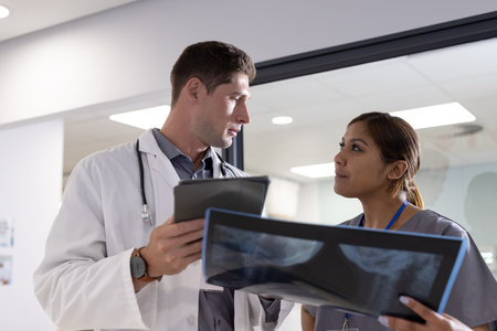 Unaltered portrait of diverse male and female doctor with tablet and x ray in hospital corridor....