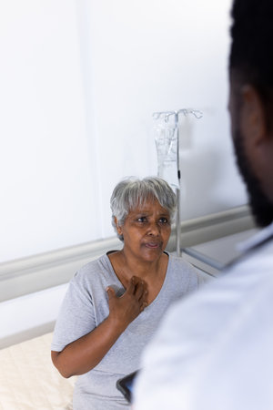 Concerned senior biracial female patient talking with diverse male doctor in hospital. Hospital,...
