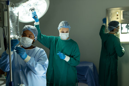 Two diverse female surgical techs adjusting light and iv bag in operating theatre during operation. Hospital, medical and healthcare services.の写真素材