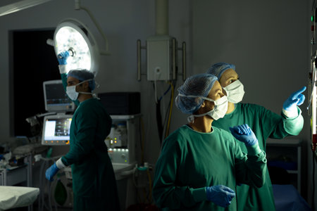 Two diverse female surgeons discussing x-ray in operating theatre, with colleague in background. Hospital, medical and healthcare services.の写真素材