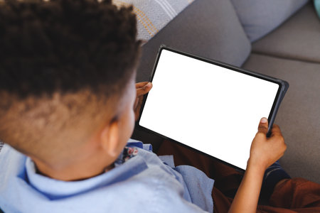 African american boy sitting on sofa, using tablet with copy space in living room. Technology,...