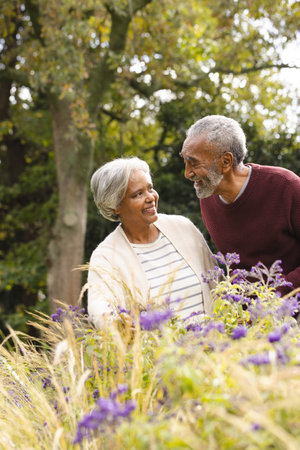 Happy senior biracial couple holding hands and smiling at each other in garden at home. Senior...