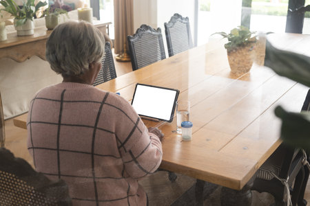 Senior biracial woman having video call at home with doctor on tablet with copy space. Senior lifestyle, retirement, communication, telemedicine and domestic life, unaltered.の写真素材