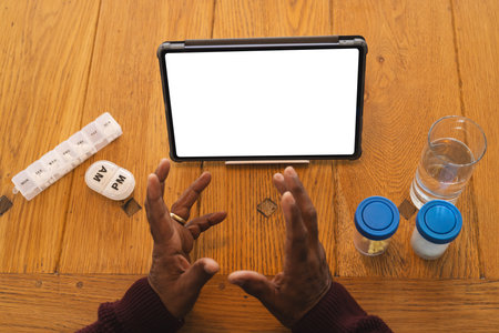 Senior biracial man having video call with doctor on tablet with copy space, at home. Senior lifestyle, retirement, communication, telemedicine and domestic life, unaltered.の写真素材