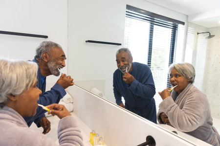Happy senior biracial couple wearing bathrobes and brushing teeth in bathroom at home. Senior lifestyle, retirement, selfcare and domestic life, unaltered.の写真素材