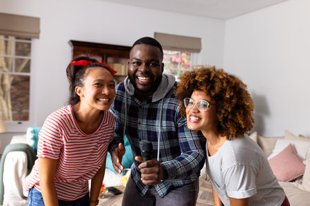 Portrait of happy diverse friends dancing and karaoke singing with microphone at home. Domestic life, friendship, music and lifestyle, unaltered.の写真素材