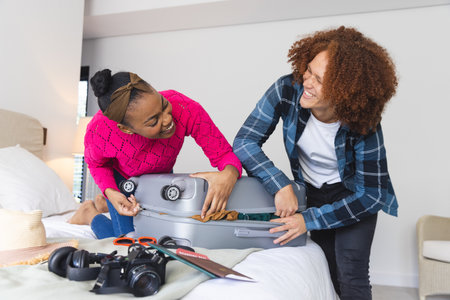 Happy diverse couple closing packed suitcase together in bedroom, at home. Travel, vacations, preparation, lifestyle and free time, unaltered.の写真素材