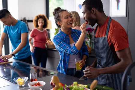 Happy diverse group of friends cooking and talking with drinks in kitchen. Domestic life, friendship, togetherness, food and lifestyle, unaltered.の写真素材