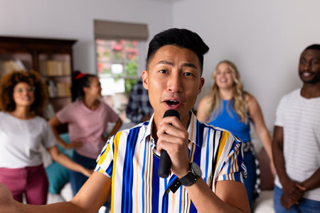 Portrait of happy diverse friends dancing and karaoke singing with microphone at home. Domestic life, friendship, music and lifestyle, unaltered.の写真素材