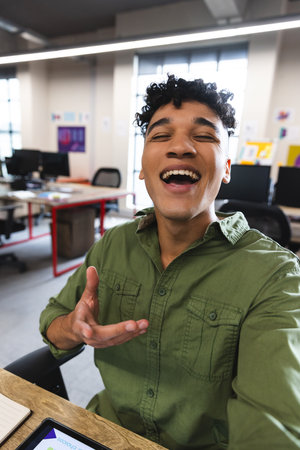 Biracial man smiling looking at the camera on smartphone during a video call at office. Business, technology and office conceptの写真素材
