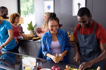 Happy diverse group of friends cooking and talking with drinks in kitchen. Domestic life, friendship, togetherness, food and lifestyle, unaltered.の写真素材
