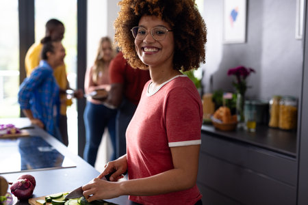 Portrait of happy biracial woman cutting vegetables with diverse friends in kitchen. Domestic life, friendship, togetherness, food and lifestyle, unaltered.の写真素材