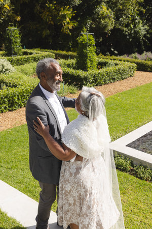 Happy senior biracial bride and groom dancing in garden at sunny wedding ceremony, copy space.の写真素材