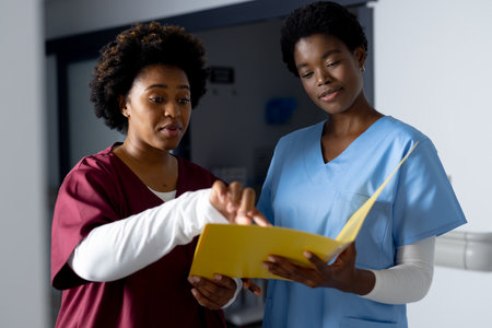 African american female doctors holding documents and discussing work in corridor at hospital. Hospital, teamwork, medicine, healthcare and work, unaltered.の写真素材