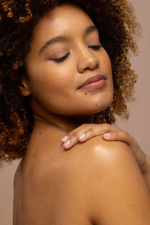 Biracial woman with dark curly hair smiling with eyes closed and hand on shoulder. Femininity, face, facial expressions, body, skin and beauty, unaltered.の写真素材