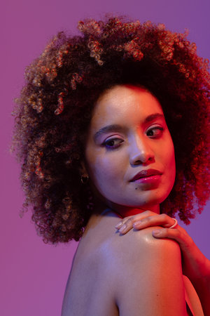 Biracial woman with curly hair with hand on shoulder on purple background. Femininity, face, facial...