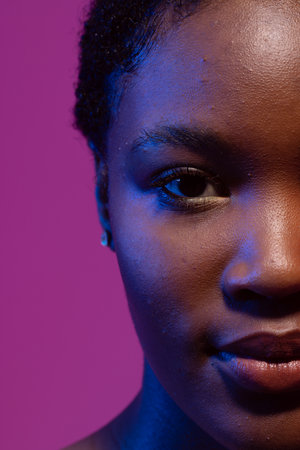 Half portrait of african american woman with short hair in blue light, purple background. Femininity, face, facial expressions, body, skin, makeup, fashion and beauty, unaltered.の写真素材